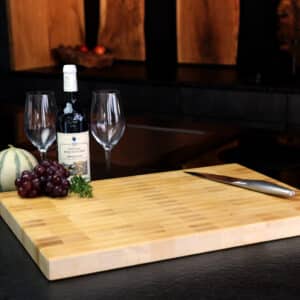 Birch end grain cutting board in modern kitchen, high quality knives and grapes, and wine decoration in the background